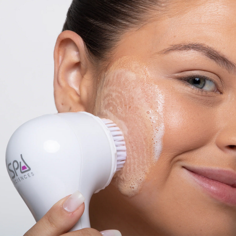 A woman is using a Spa Sciences Face Cleanse brush to clean her face.