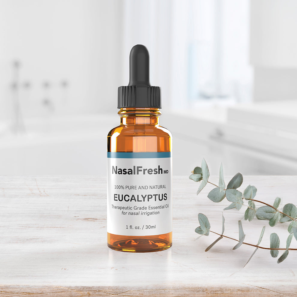 A bottle of Spa Sciences Therapeutic Grade Eucalyptus Essential Oil, celebrated for its mucus solvent properties, sits with a dropper on the bathroom counter beside eucalyptus leaves.