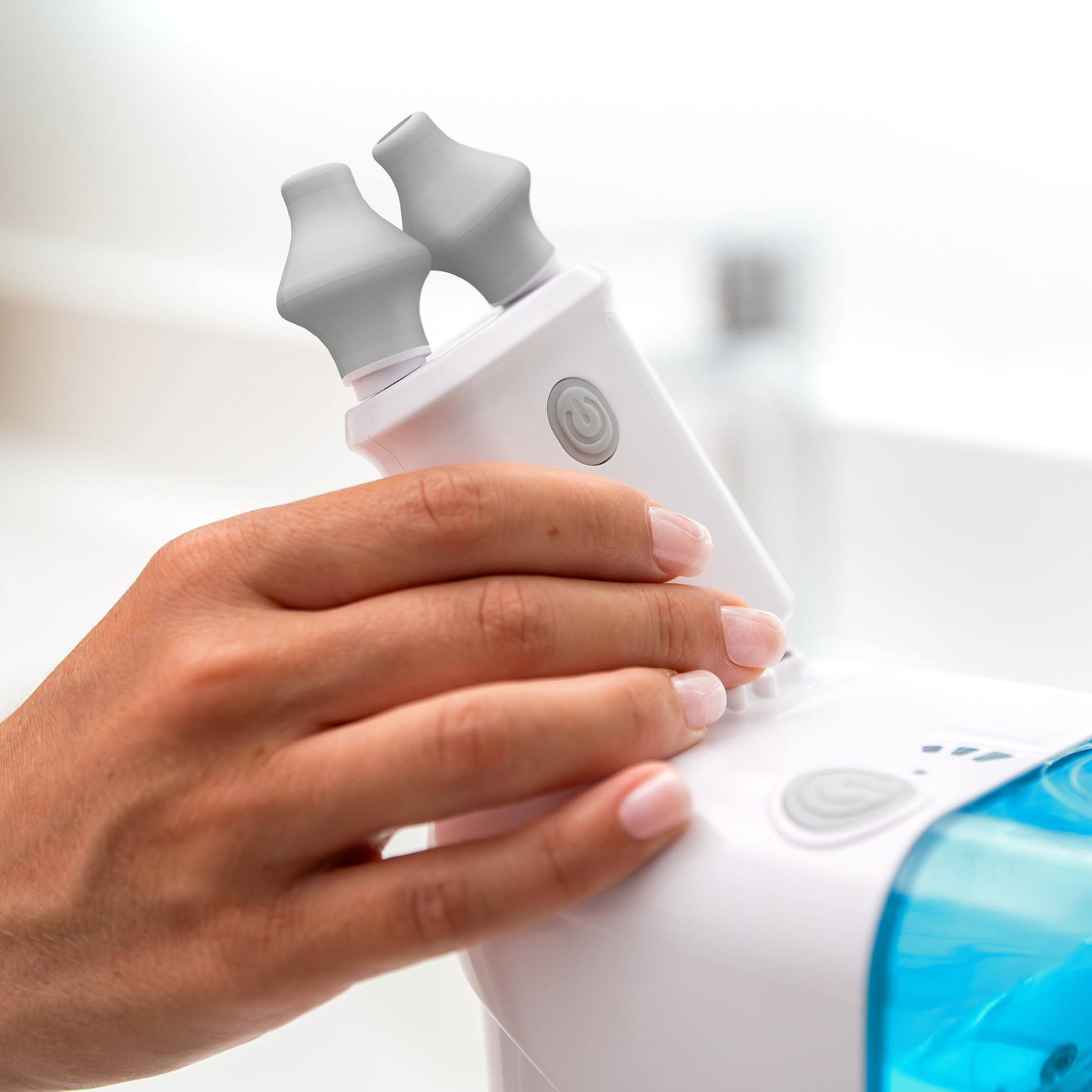 A person adjusts a Spa Sciences NasalFresh MD nasal device with two gray silicone nose pillows on a base featuring a blue water chamber, utilizing the Pair of Replacement Nose Pillows.