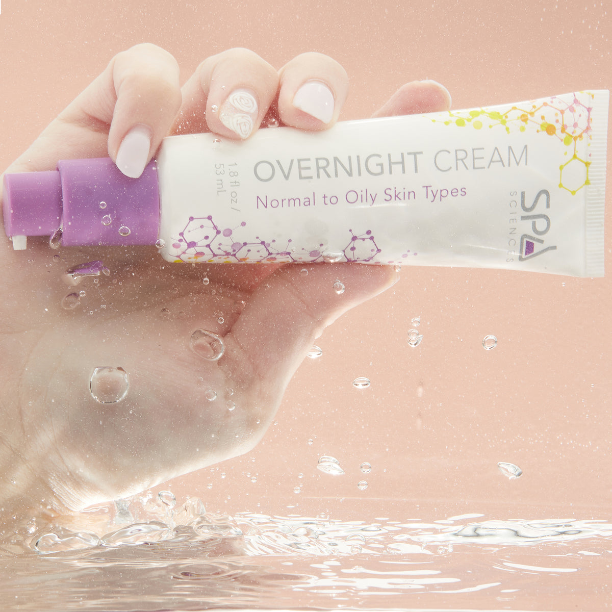 A hand holds a tube of Spa Sciences Shine Control System overnight cream for normal to oily skin types, surrounded by splashing water droplets.