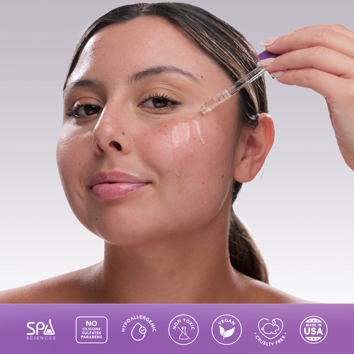 A person applies a Spa Sciences Skin Cycling Kit (Dry Skin) serum from a glass dropper onto their cheek above icons denoting that the product is vegan, cruelty-free, and free of silicones and parabens.
