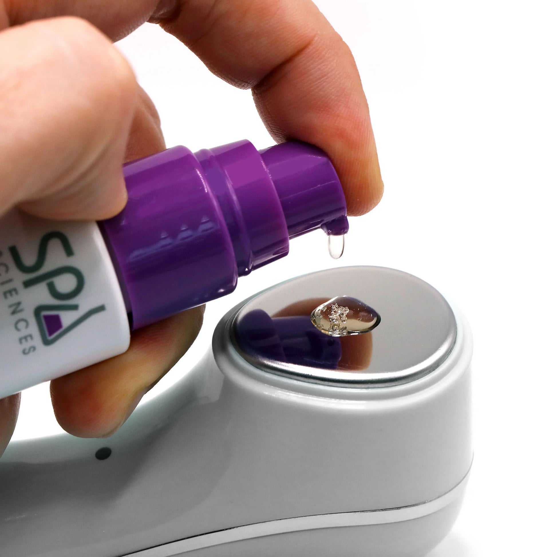 A hand dispenses serum from Spa Sciences' Ultimate Moisture Bundle’s purple pump bottle onto the metal head of a gray handheld skincare device.