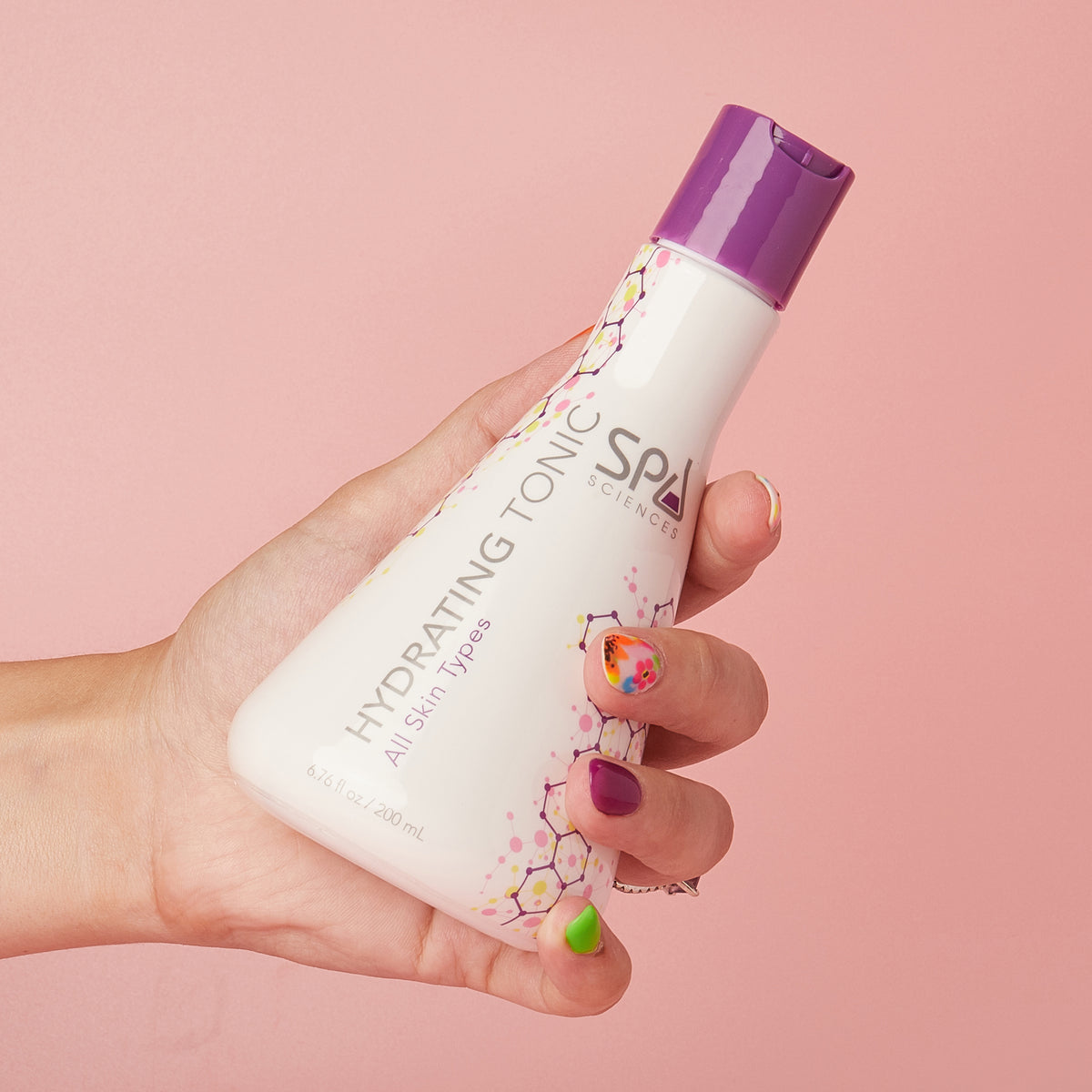 A hand holds a white bottle of hydrating tonic from the Ultimate Self-Care Set by Spa Sciences, featuring a purple cap.