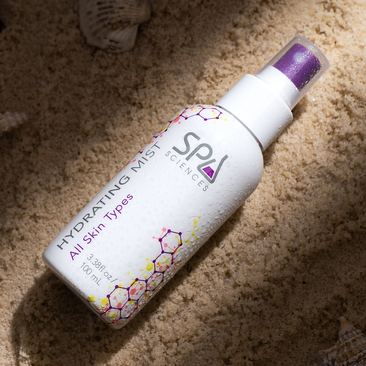 A spray bottle of hydrating mist from the Ultimate Self-Care Set resting on sand.