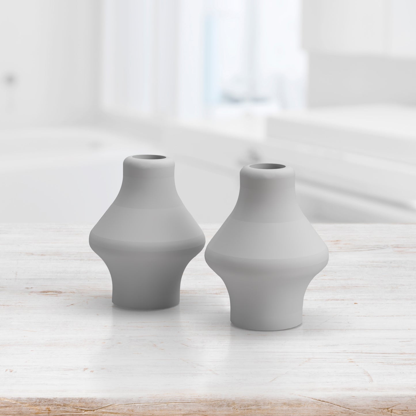 Two contemporary, grey, vase-shaped objects are placed next to each other on a wooden surface in a bright room, reminiscent of the sleek Pair of Replacement Nose Pillows from Spa Sciences.