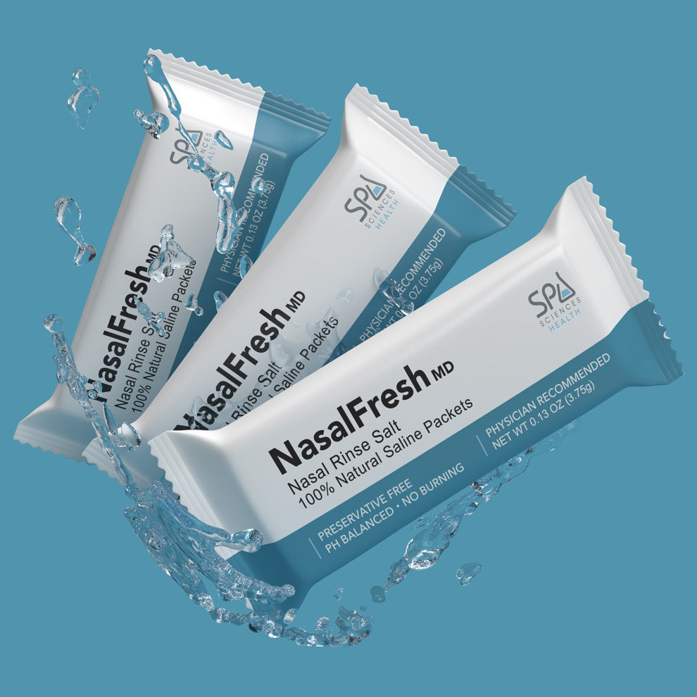 Three NasalFresh MD Formulated Nasal Rinse Salt packets from Spa Sciences are depicted with water splashing around them against a blue background. The packaging indicates they contain 100% natural saline and are preservative-free, offering effective sinus relief through gentle nasal irrigation.