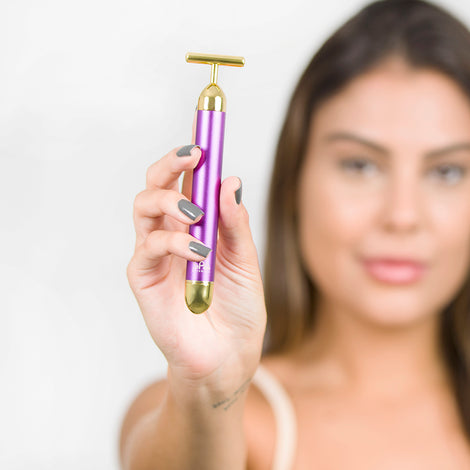 A woman holding up a Spa Sciences GOLD BAR, a facial tool.