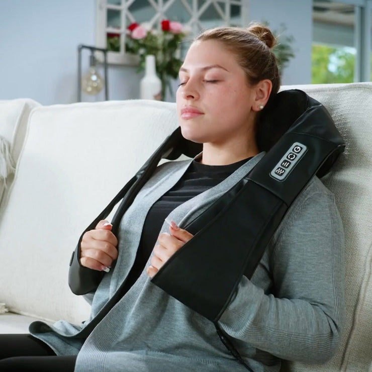 A woman is sitting on a couch with a Spa Sciences TESA neck massager.